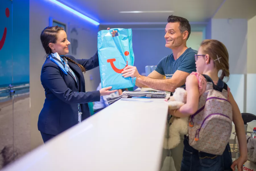 TUI baliebediende geeft TUI tas aan een vader met dochter